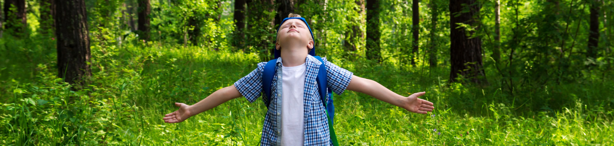 Glückliches Kind, das im grünen Wald spazieren geht und frische Luft atmet